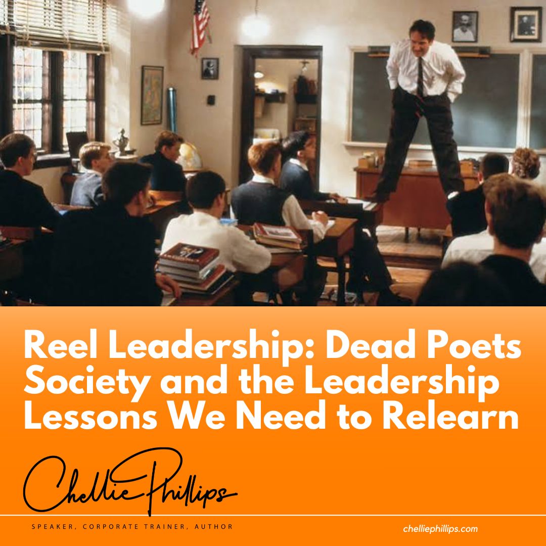 An adult leader stands on a desk in a traditional classroom as professionals consider a new perspective.
